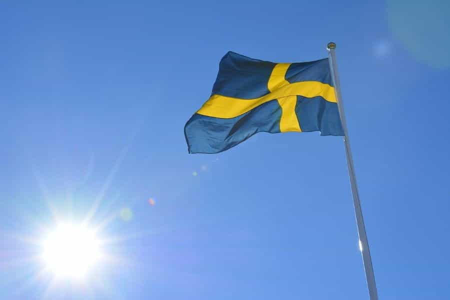 The Swedish flag flying with the sky and sun in the background.
