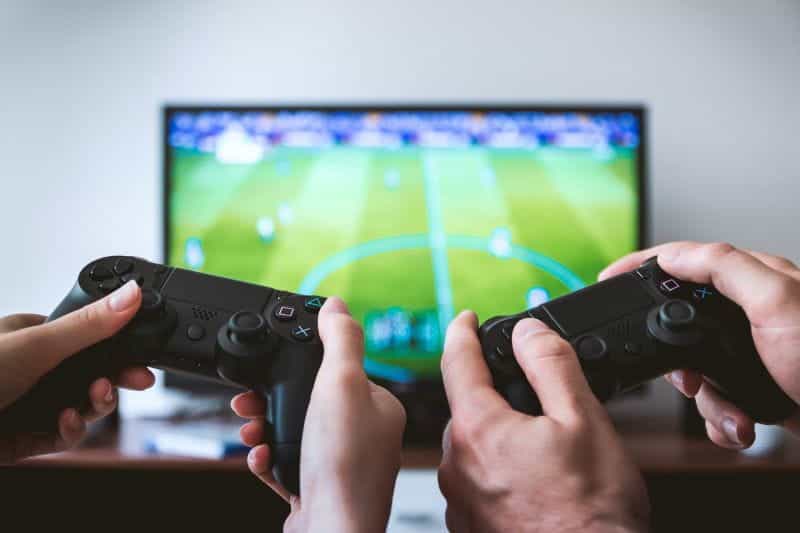 Two people hold games controllers in front of a football video game.