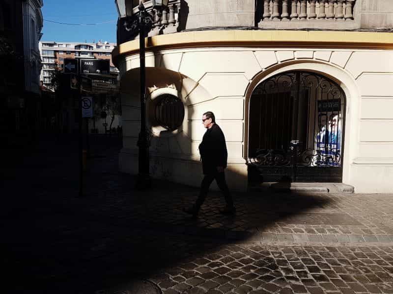 A man walks on a stone walkway near a white concrete building in Santiago, Chile.